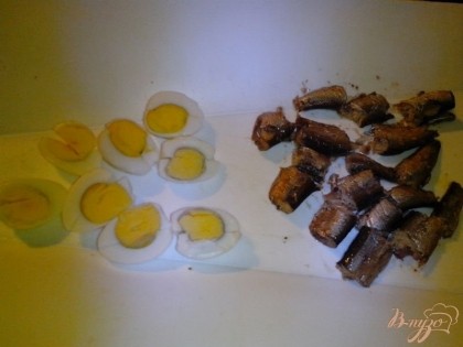 Нарезать охлаждённые яйца вдоль на четыре части. А шпроты - на кусочки среднего размера.