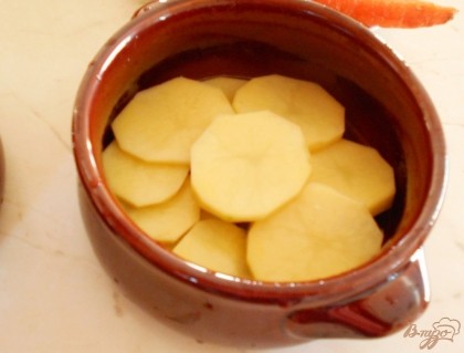 На дно горшка выкладываем картофель, нарезанный тонкими кружочками.