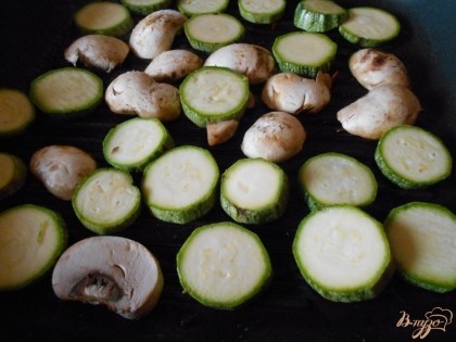 Цукини и грибы- шампиньоны нарезаем  кольцами и продольными платинами. Обжариваем овощи на сковородке гриль до  готовности.