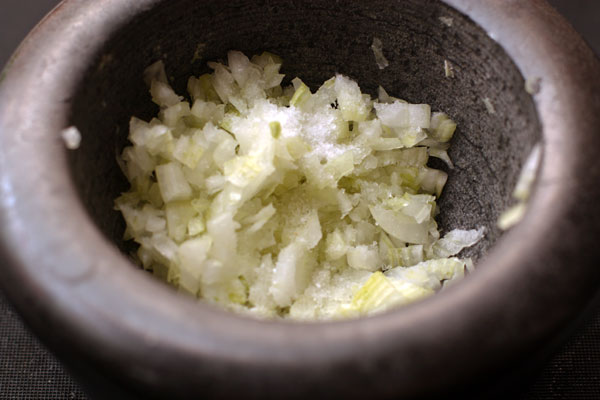 Переложите лук в ступку и слегка разотрите его с крупной солью и мелко нарезанными листьями кинзы.