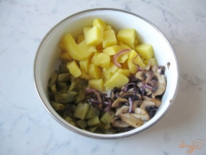 В миску выкладываем нарезанные картофель, солёный огурец, лук и лук тушеный с грибами. Перемешиваем.
