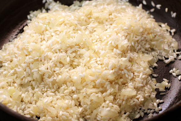 Добавьте рис в сковороду, перемешайте и готовьте 2-3 минуты, пока рис не покроется маслом и не станет полупрозрачным.
