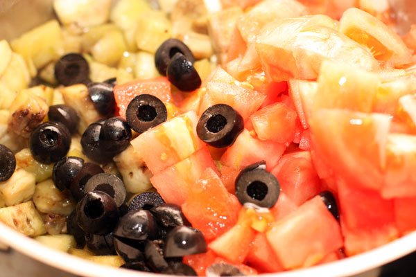 Добавьте к баклажанам нарезанные помидоры, маслины и каперсы, уменьшите огонь и тушите без крышки, пока овощи не станут мягкими. 